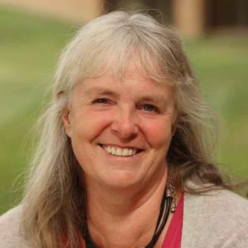 Older white woman with blond and grey hair wearing a tan sweater smiling at the camera