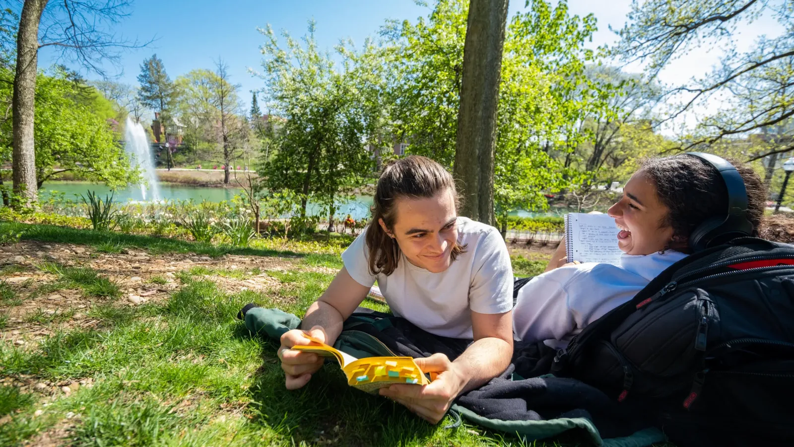 Two students resting near mirror lake while laughing and reading.