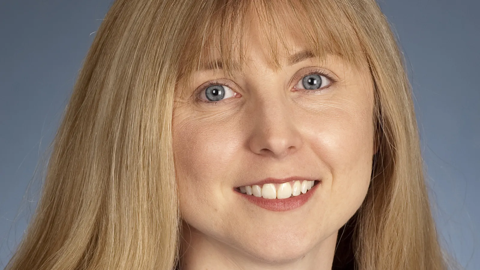Image of white woman with blond hair, wearing a blue blouse smiling at the camera