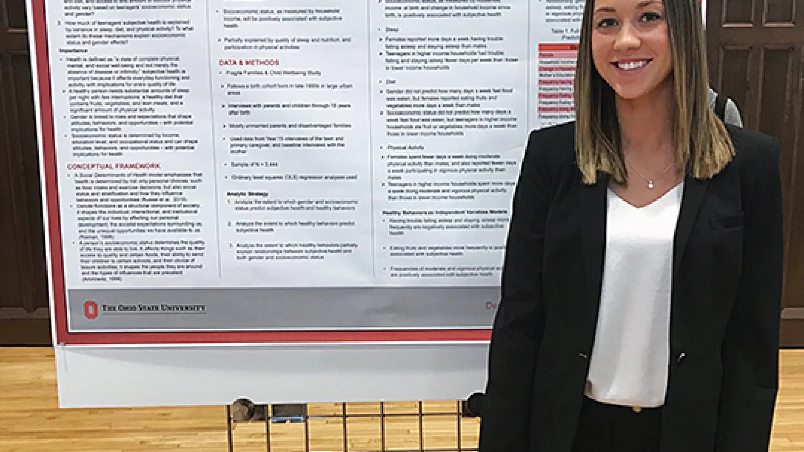 White female in black suit standing in front of poster