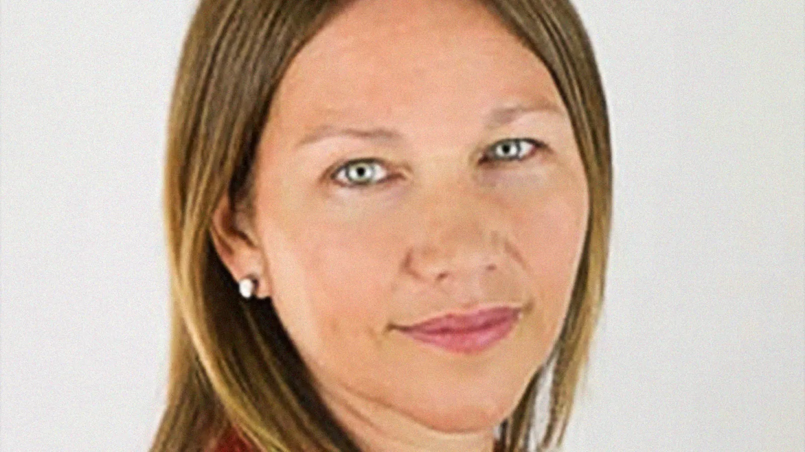 White female professor, turned toward camera smiling, wearing a red blazer.
