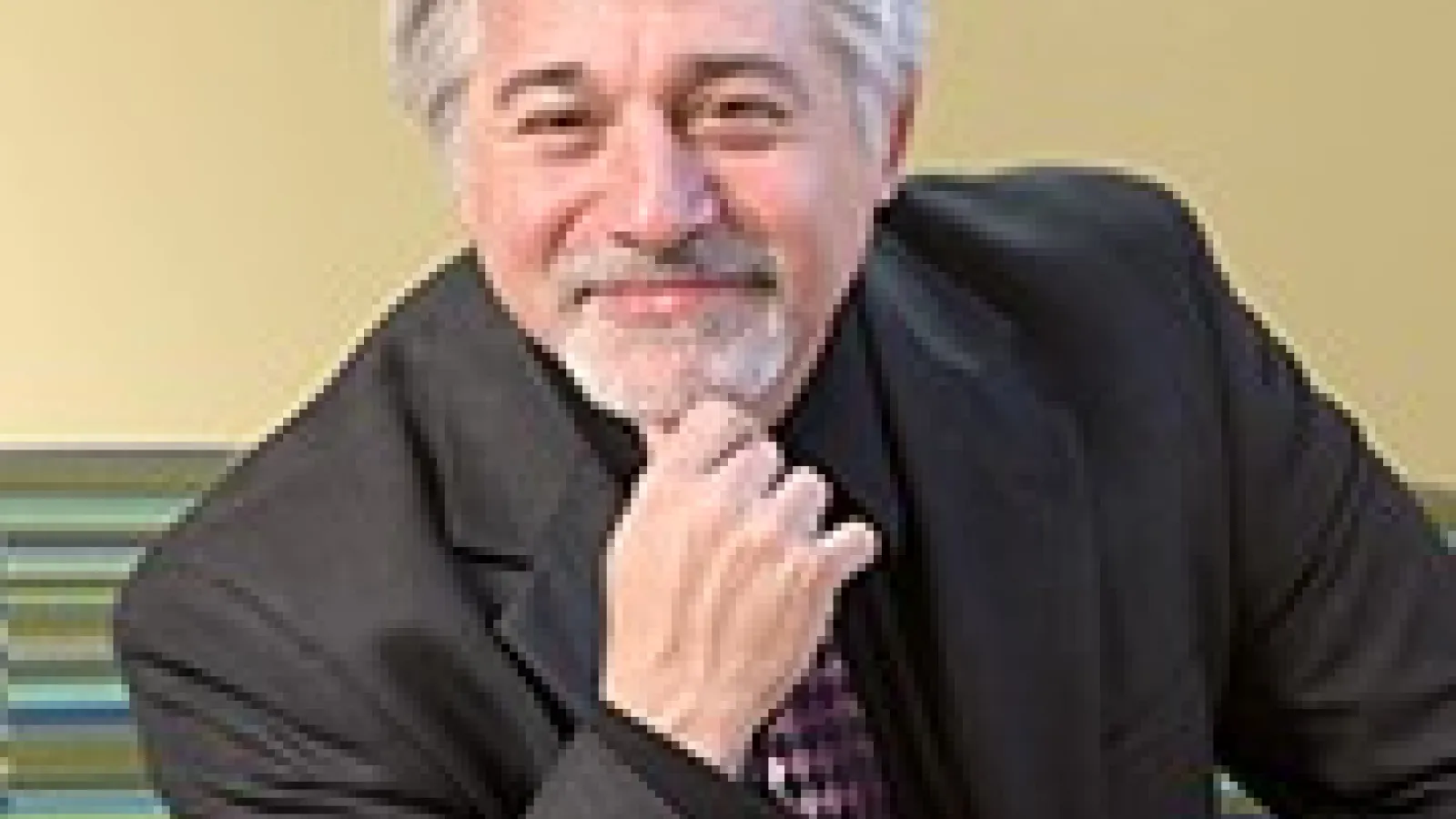 White man in grey suit with grey hair and beard, smiling at camera