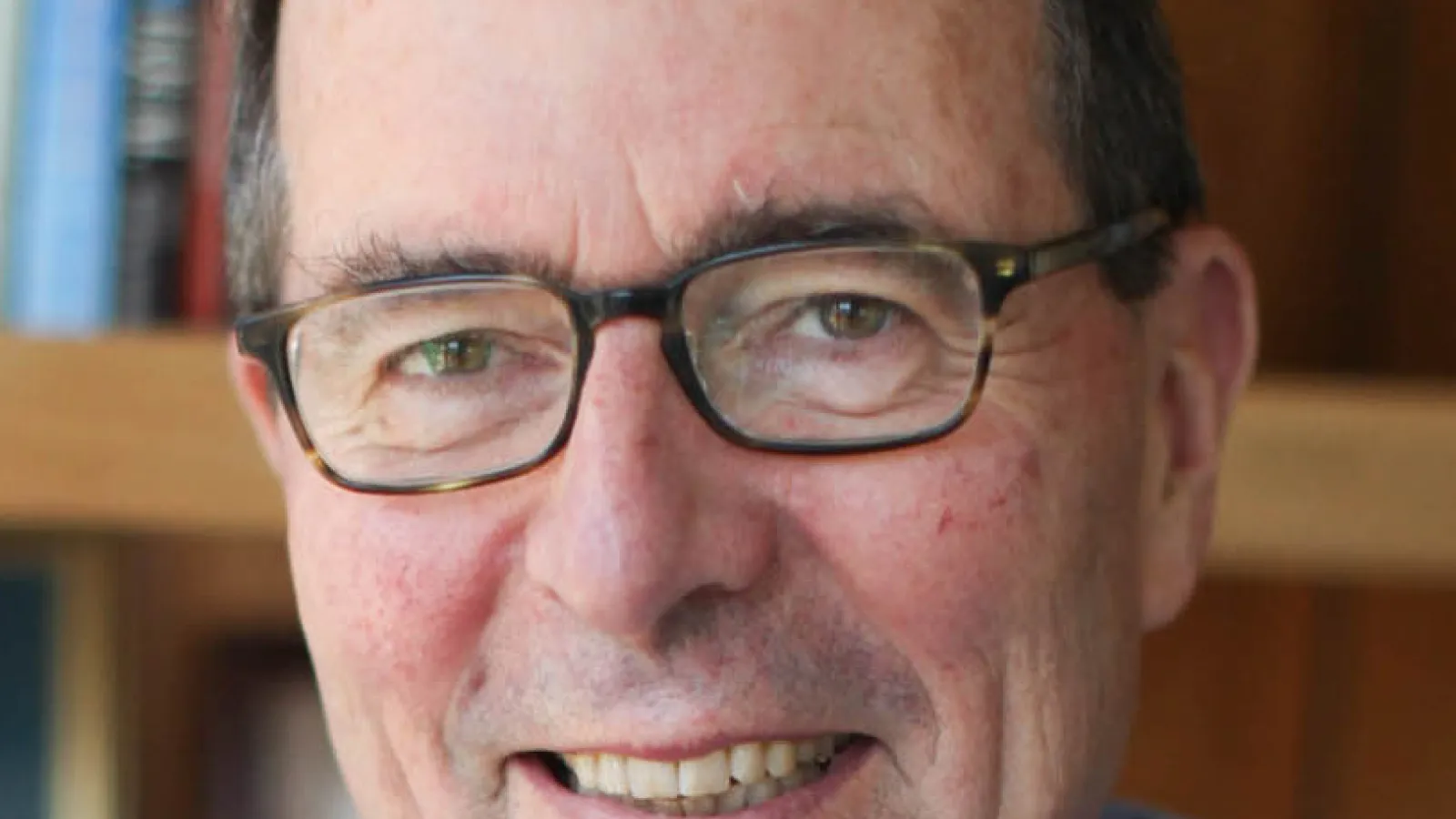 Image of white man with brown hair and glasses, wearing a blue shirt smiling at the camera