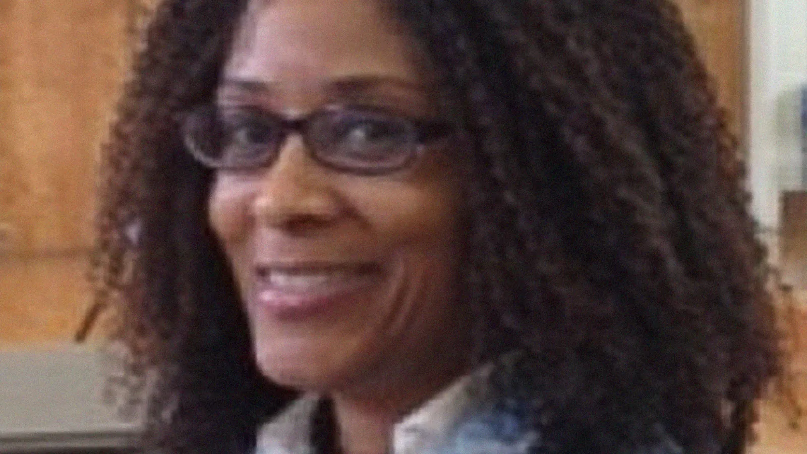 Black female professor, turned toward the camera smiling. She is wearing a blue jacket.