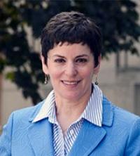 White woman with dark short hair, wearing a striped shirt and blue blazer, smiling at camera