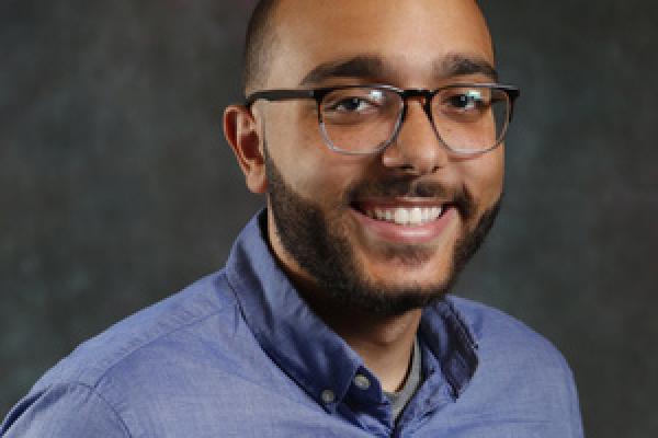 Black male smiling at camera, wearing a blue shirt and glasses