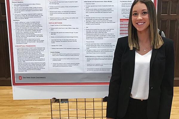 White female in black suit standing in front of poster