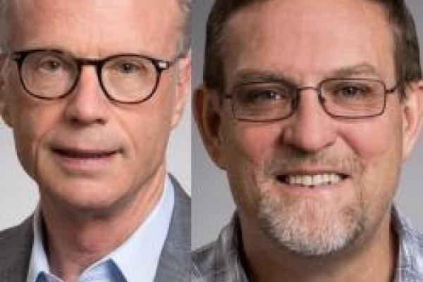 Image of two white men, both wearing glasses and blue button down shirts smiling at the camera