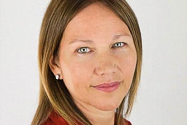 White female professor, turned toward camera smiling, wearing a red blazer.