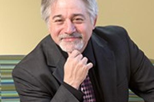 White man in grey suit with grey hair and beard, smiling at camera