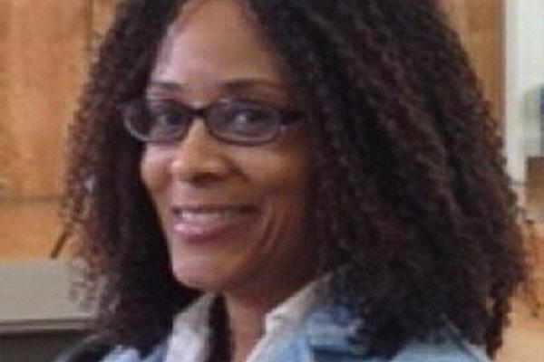 Black female professor, turned toward the camera smiling. She is wearing a blue jacket.