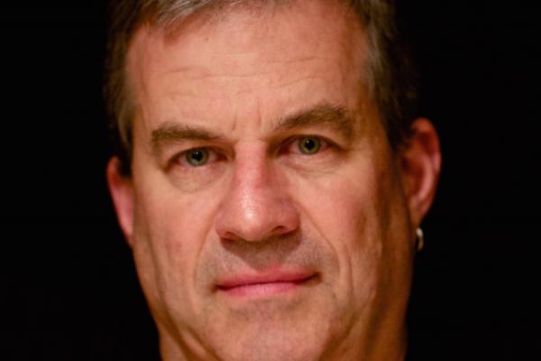 Author Sam Quinones Image of a white man, looking at camera with a flat look on his face, against a back background