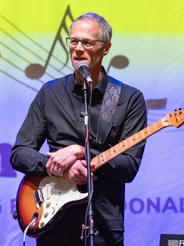 Bill Macdonald holding a guitar at Rocking with the Dean event